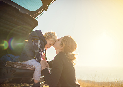 mother kissing son who's sitting in the back of a car